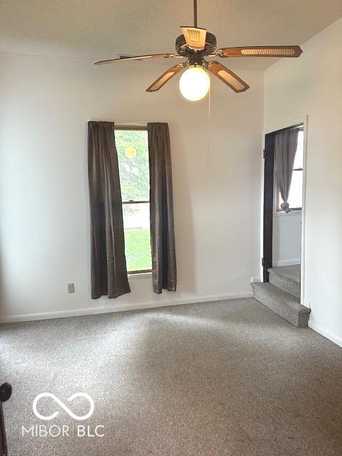 carpeted empty room featuring a ceiling fan, stairs, and baseboards