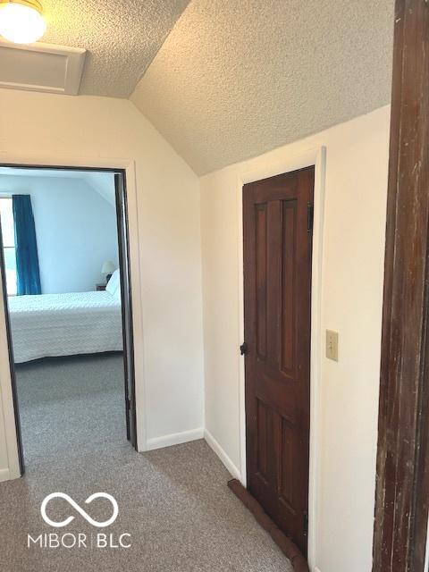 hall with baseboards, carpet flooring, a textured ceiling, and vaulted ceiling