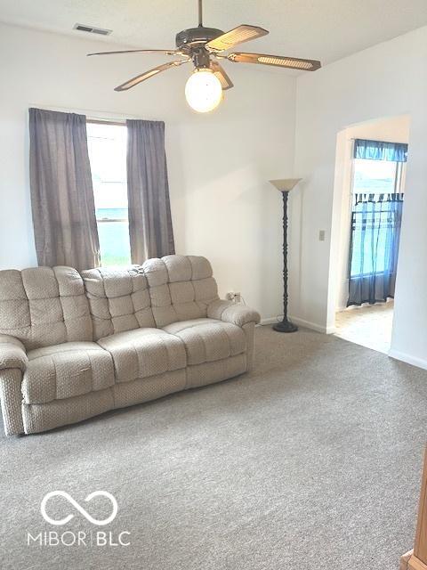living area with carpet flooring, visible vents, baseboards, and a ceiling fan