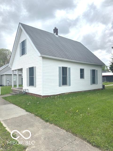 view of side of property featuring roof with shingles, a chimney, and a lawn