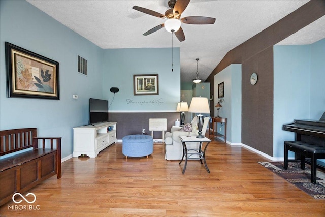 living room featuring visible vents, baseboards, ceiling fan, light wood-type flooring, and a textured ceiling