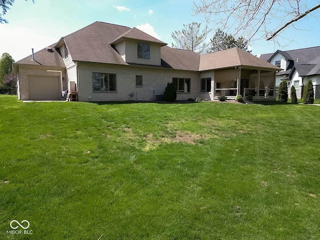 back of house with brick siding, an attached garage, a yard, and a sunroom