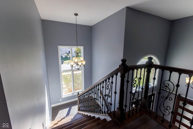 staircase featuring an inviting chandelier, wood finished floors, and a healthy amount of sunlight