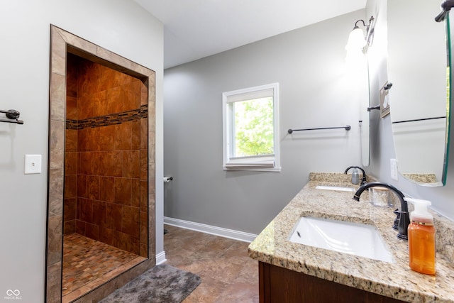 full bath with a sink, baseboards, a tile shower, and double vanity