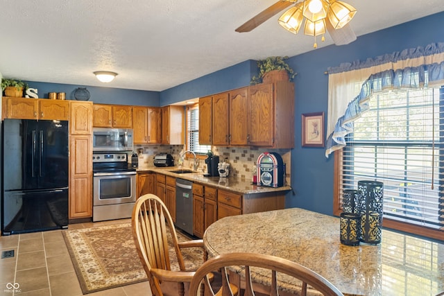 kitchen featuring decorative backsplash, brown cabinetry, a ceiling fan, appliances with stainless steel finishes, and a sink
