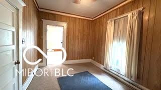 carpeted empty room with crown molding, ceiling fan, and wooden walls