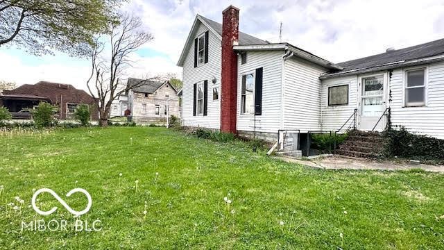 view of side of property with a lawn, a chimney, and entry steps