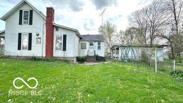 rear view of house featuring a lawn, fence, and a chimney