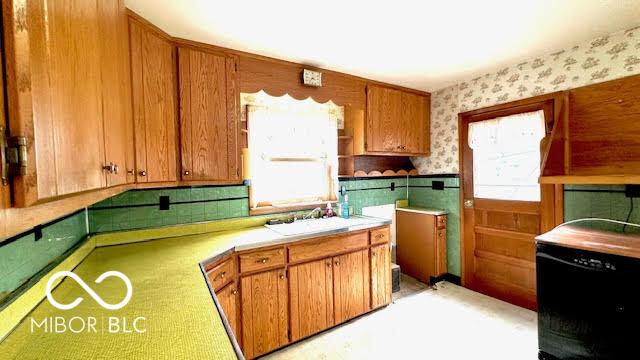 kitchen with a sink, plenty of natural light, wainscoting, and wallpapered walls