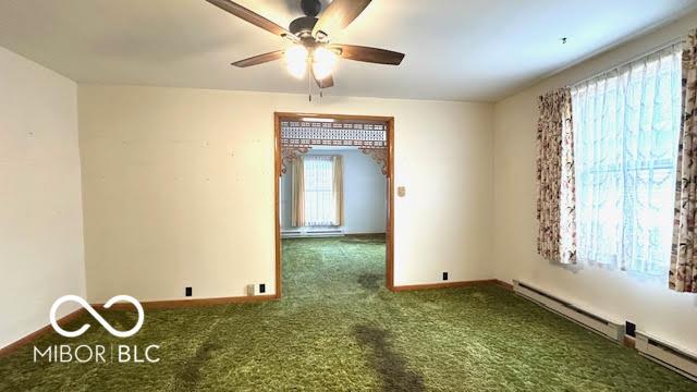 carpeted empty room with baseboards, a ceiling fan, and baseboard heating
