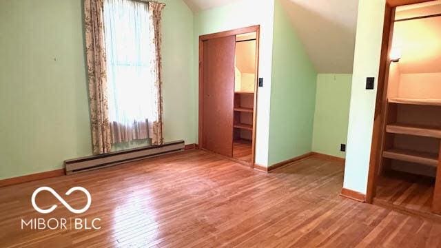unfurnished bedroom with wood finished floors, baseboards, lofted ceiling, and baseboard heating