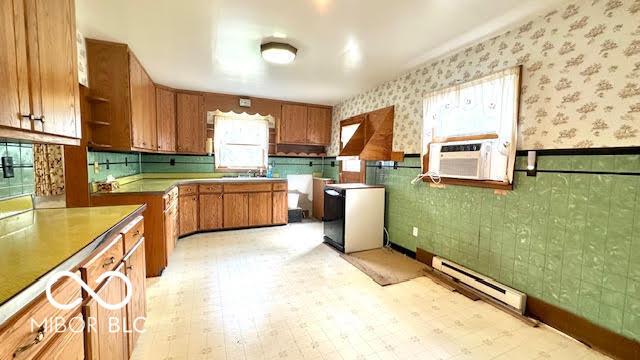 kitchen featuring brown cabinetry, open shelves, baseboard heating, wallpapered walls, and a wainscoted wall