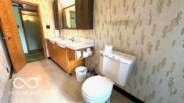 bathroom with vanity, baseboards, toilet, and wallpapered walls