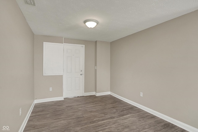 empty room featuring a textured ceiling, visible vents, dark wood-style floors, and baseboards