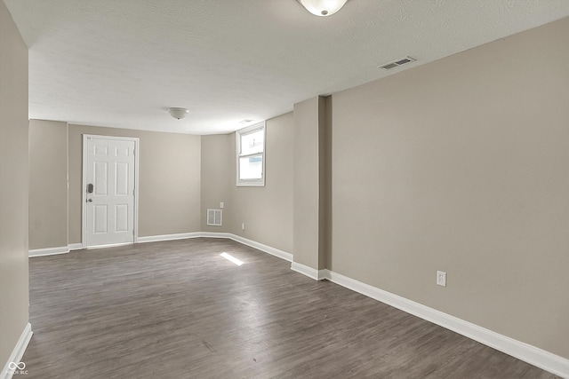 spare room with dark wood-style floors, a textured ceiling, visible vents, and baseboards