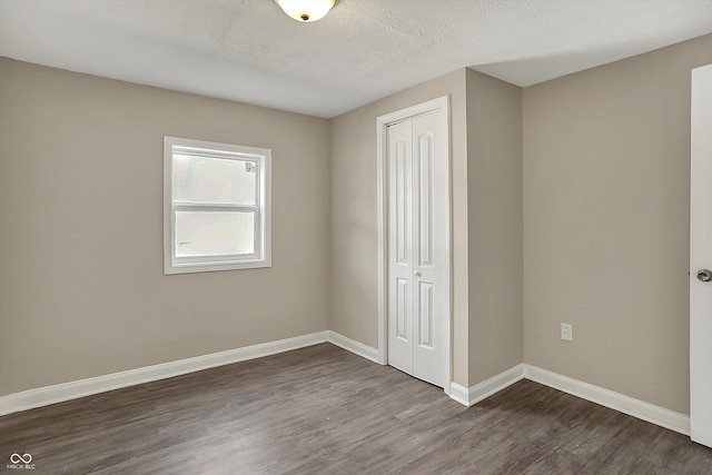 unfurnished bedroom with baseboards, dark wood finished floors, and a closet