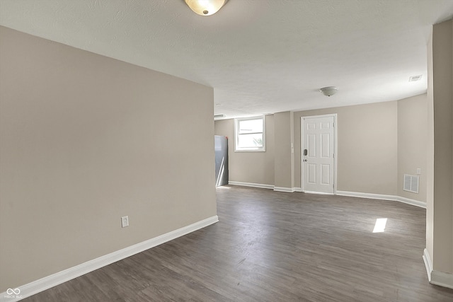 spare room featuring dark wood finished floors, visible vents, a textured ceiling, and baseboards