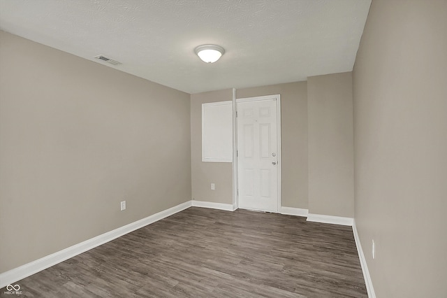 spare room with a textured ceiling, visible vents, dark wood-style floors, and baseboards