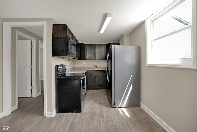 kitchen with freestanding refrigerator, a sink, baseboards, light wood-type flooring, and black electric range oven