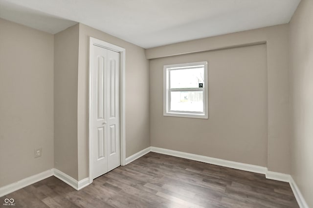 unfurnished bedroom featuring dark wood-style floors, a closet, and baseboards