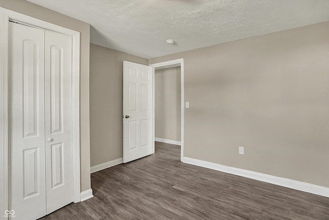 unfurnished bedroom featuring dark wood finished floors, a closet, a textured ceiling, and baseboards