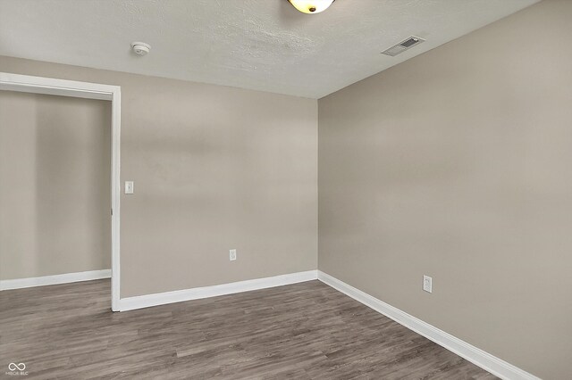 spare room with dark wood-style flooring, visible vents, a textured ceiling, and baseboards