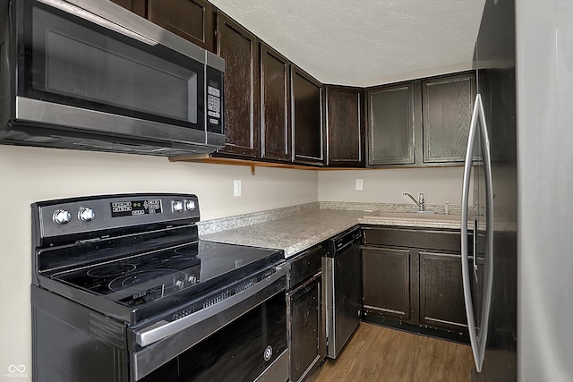 kitchen with light wood-style flooring, appliances with stainless steel finishes, light countertops, dark brown cabinets, and a sink