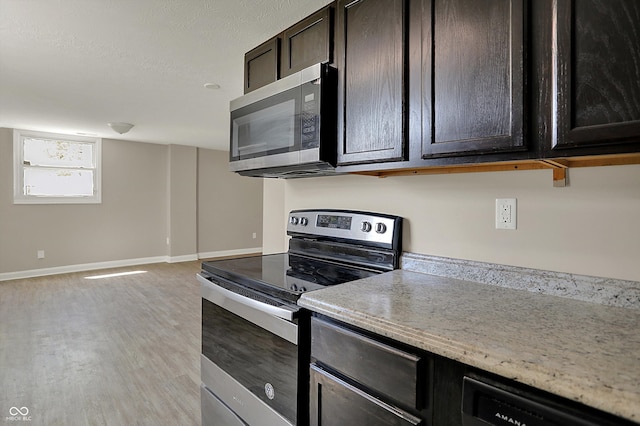kitchen with stainless steel appliances, light wood-type flooring, dark brown cabinetry, light stone counters, and baseboards