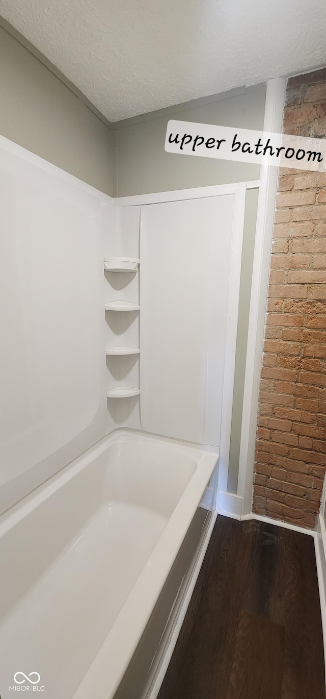 bathroom with a textured ceiling, brick wall, a bathtub, and wood finished floors