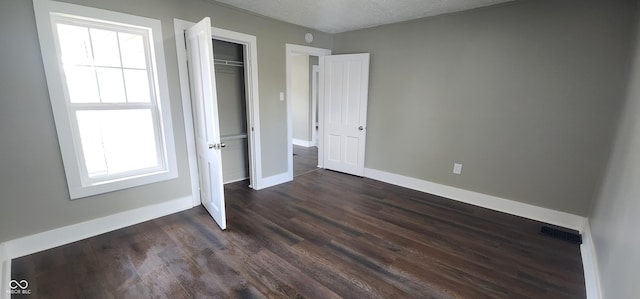 unfurnished bedroom featuring a closet, a textured ceiling, visible vents, baseboards, and dark wood-style floors