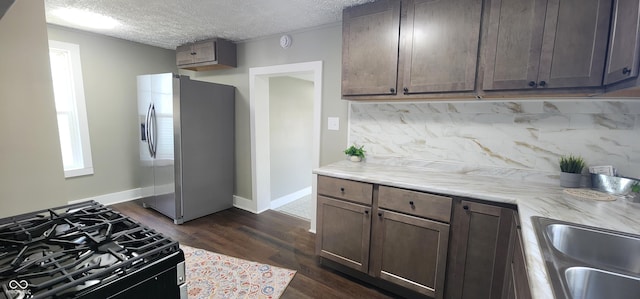 kitchen with a sink, tasteful backsplash, dark wood-type flooring, black range with gas cooktop, and stainless steel fridge