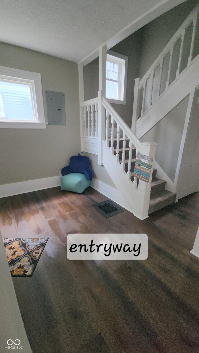 stairs featuring baseboards, a healthy amount of sunlight, electric panel, and wood finished floors