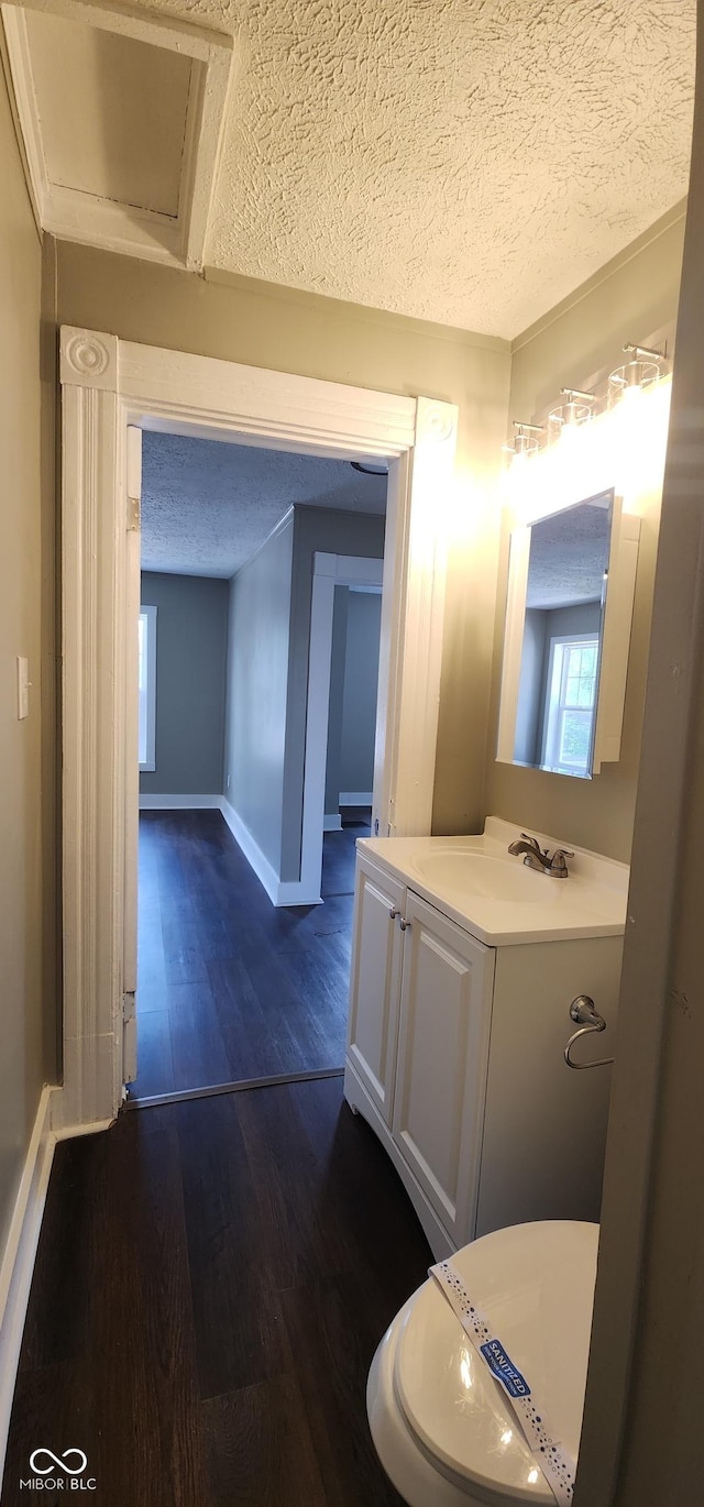 half bathroom featuring baseboards, vanity, a textured ceiling, and wood finished floors