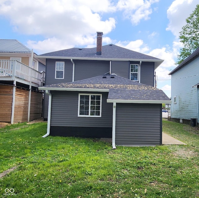 rear view of property featuring a shingled roof, a chimney, and a lawn