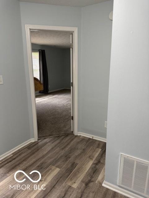 hall with visible vents, baseboards, and wood finished floors