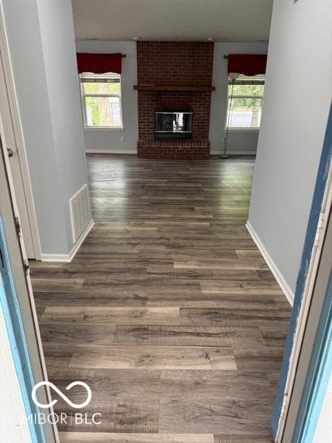 unfurnished living room with a brick fireplace, baseboards, visible vents, and wood finished floors