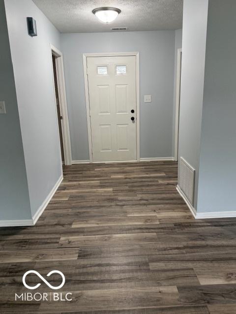 interior space with baseboards, a textured ceiling, dark wood-type flooring, and visible vents