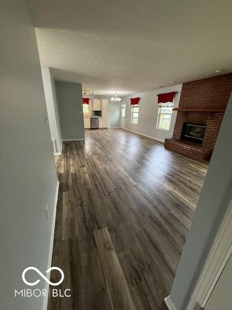 unfurnished living room featuring baseboards, a brick fireplace, dark wood finished floors, and a notable chandelier