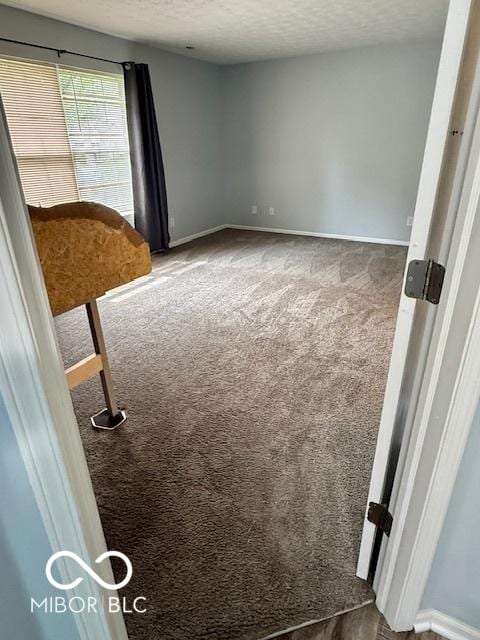 empty room featuring carpet floors, a textured ceiling, and baseboards