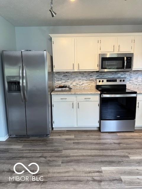 kitchen featuring decorative backsplash, wood finished floors, white cabinetry, light stone counters, and stainless steel appliances