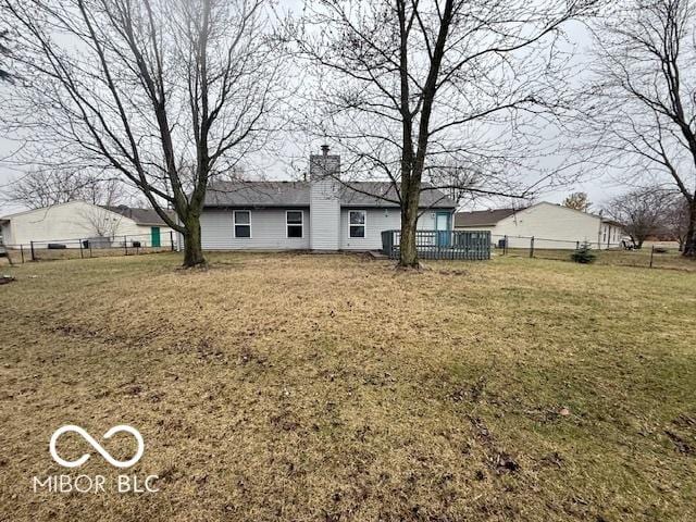 back of house featuring fence, a yard, and a chimney