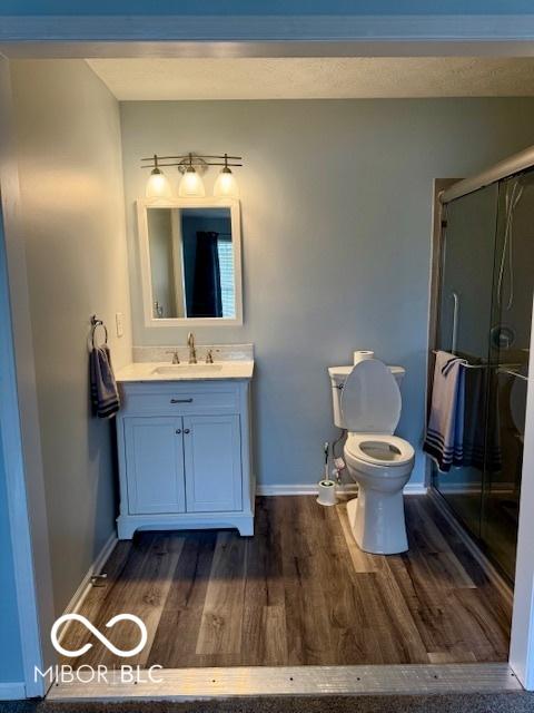 full bathroom with vanity, wood finished floors, toilet, baseboards, and a stall shower
