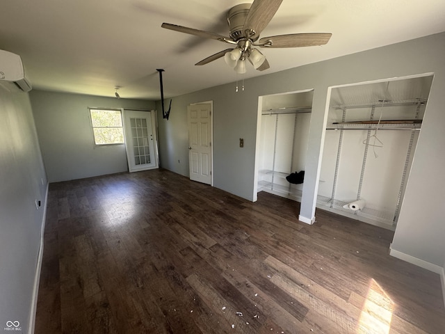 unfurnished bedroom with a wall unit AC, a ceiling fan, wood finished floors, baseboards, and multiple closets