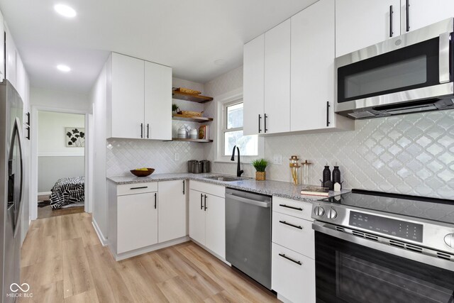 kitchen featuring light wood finished floors, light stone countertops, a sink, open shelves, and appliances with stainless steel finishes