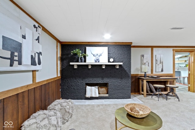carpeted living room featuring visible vents, a wainscoted wall, wood walls, and a brick fireplace