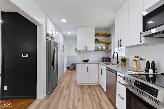 kitchen with a sink, stainless steel appliances, open shelves, light stone counters, and light wood-style flooring