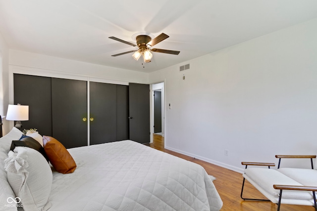 bedroom with ceiling fan, visible vents, a closet, baseboards, and wood finished floors