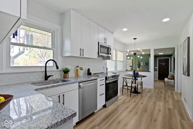 kitchen with appliances with stainless steel finishes, a chandelier, tasteful backsplash, and a sink