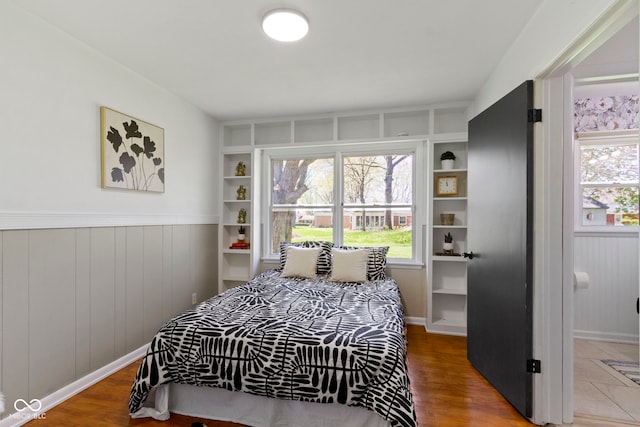 bedroom with a wainscoted wall, multiple windows, and wood finished floors