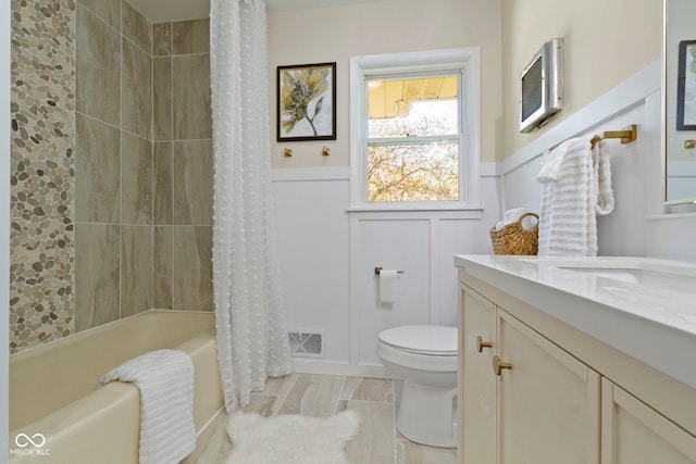 bathroom with toilet, a decorative wall, wainscoting, and vanity